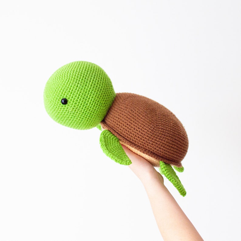 May include: A green and brown crocheted turtle toy. The turtle has a green head and legs and a brown shell.
