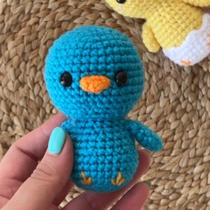 K&ouml;nnte beinhalten: Ein geh&auml;kelter blauer Vogel mit orangefarbenem Schnabel und schwarzen Augen. Der Vogel h&auml;lt seine Fl&uuml;gel seitlich ausgestreckt.