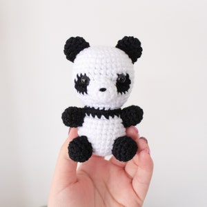 Op de afbeelding: Een klein gehaakt pandabeer speelgoed met zwart en wit bont. De panda heeft zwarte ogen en een zwarte neus.