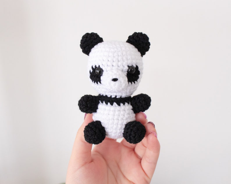 Op de afbeelding: Een klein gehaakt pandabeer speelgoed met zwart en wit bont. De panda heeft zwarte ogen en een zwarte neus.