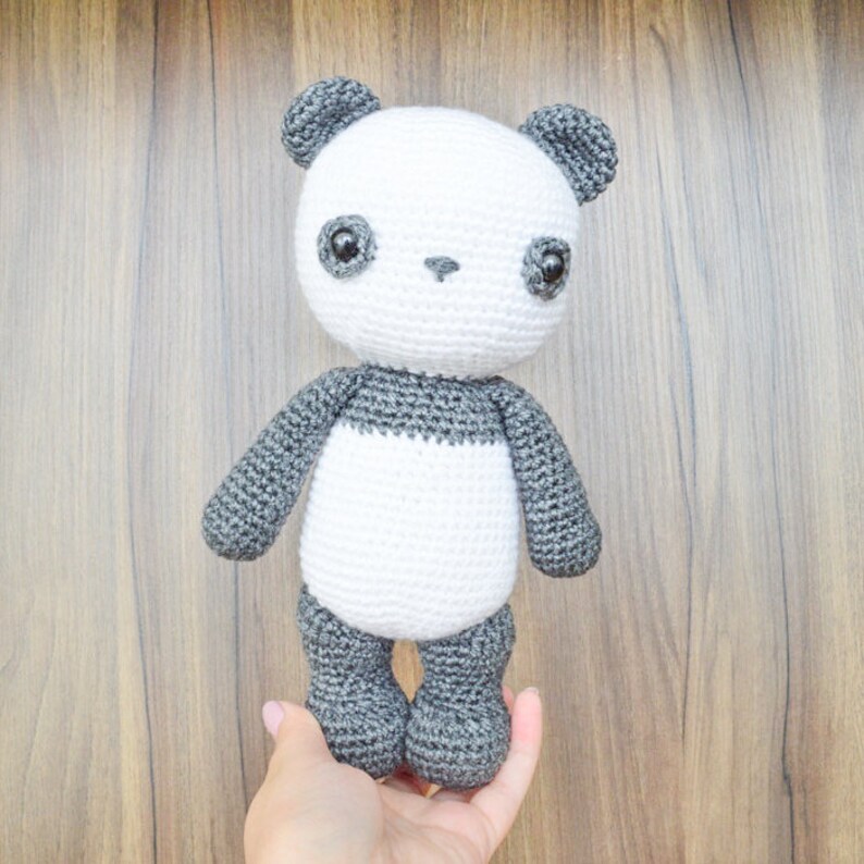 May include: A crocheted panda bear plush toy with black eyes, a white body, and gray ears, arms, and legs.