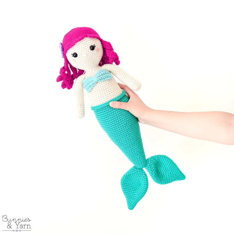 Op de afbeelding: Een gehaakte zeemeerminpop met roze haar, een blauw en wit bikini-topje en een turquoise staart.