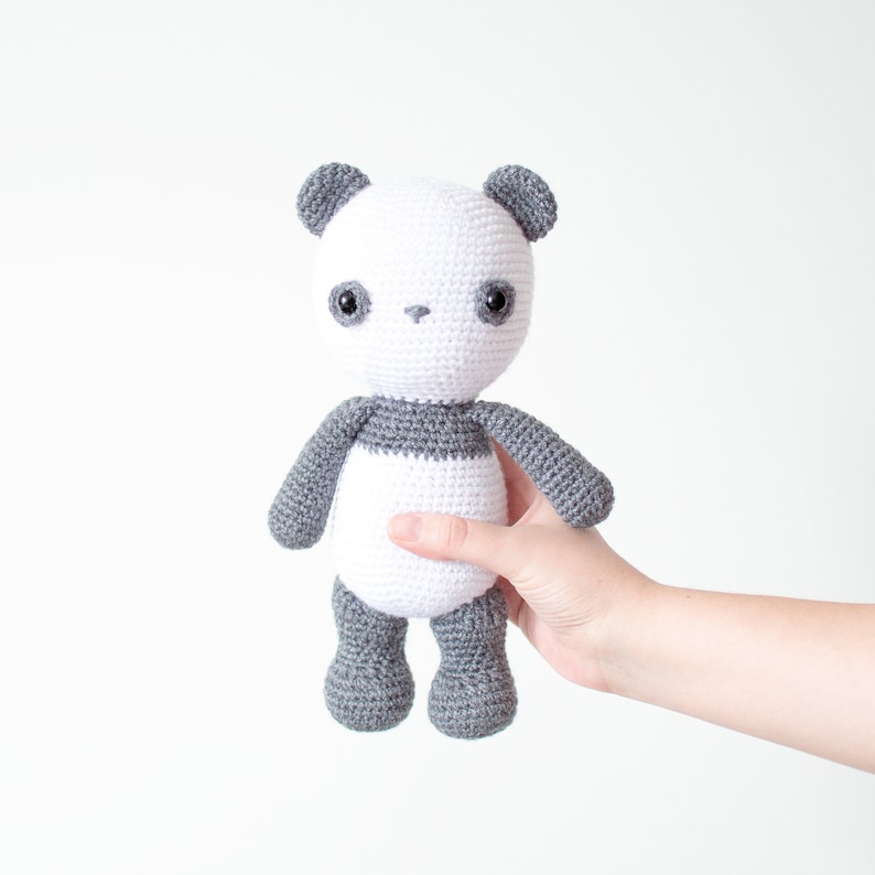 May include: A crocheted panda bear plush toy with white fur and gray accents. The panda has black eyes and a small black nose.