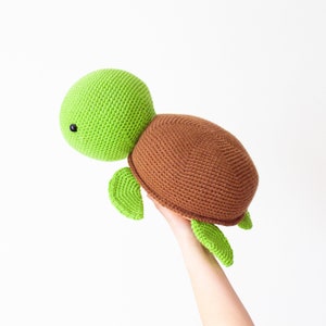 May include: A crocheted green and brown turtle toy. The turtle has a green head and legs, and a brown shell.
