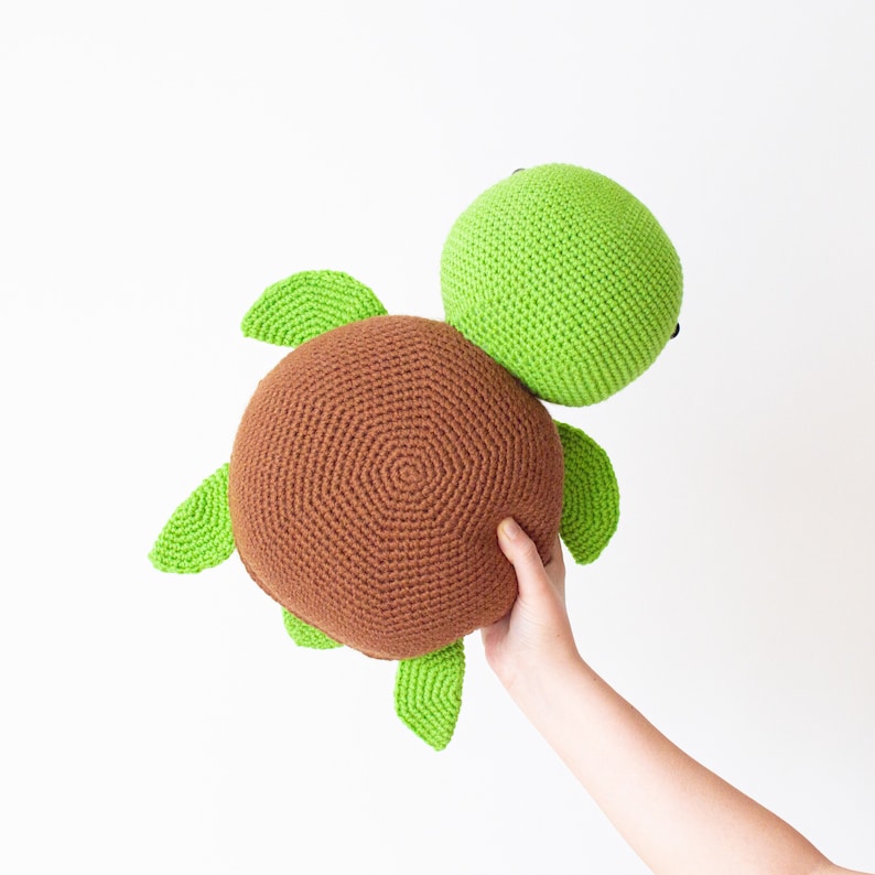 May include: A crocheted stuffed turtle toy with a brown shell and green head and limbs.