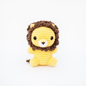 May include: A crocheted lion toy with a yellow body and brown mane. The lion has black eyes and a white nose.