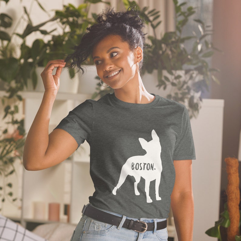 May include: Dark gray t-shirt featuring a white silhouette of a dog with the word "BOSTON" printed below. The shirt is made of a soft material and has a classic crew neck design.