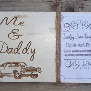May include: White wooden sign with the words "Me & Daddy" in brown lettering. A vintage car is pictured below the text. The sign has a frame for a 4x6 photo and a small card with the text "Country Livin Design Co. Holds 4x6 Photo" and contact information for Facebook and Etsy.
