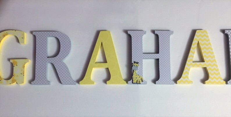 May include: Wooden letters spelling the name "GRAHAM" in yellow and grey with a small giraffe figurine on the "H".