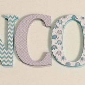 May include: Wooden letters spelling the name "LINCOLN" in light blue, gray, and white. The letters are decorated with a variety of patterns, including elephants, chevron, and polka dots.