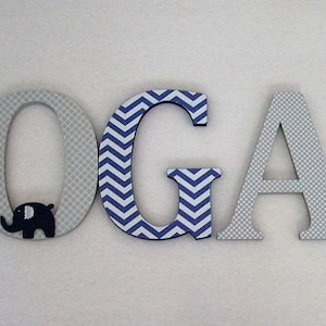 May include: Wooden letters spelling the name "LOGAN" in blue and gray. The letters are decorated with different patterns, including elephants, polka dots, and chevron stripes.