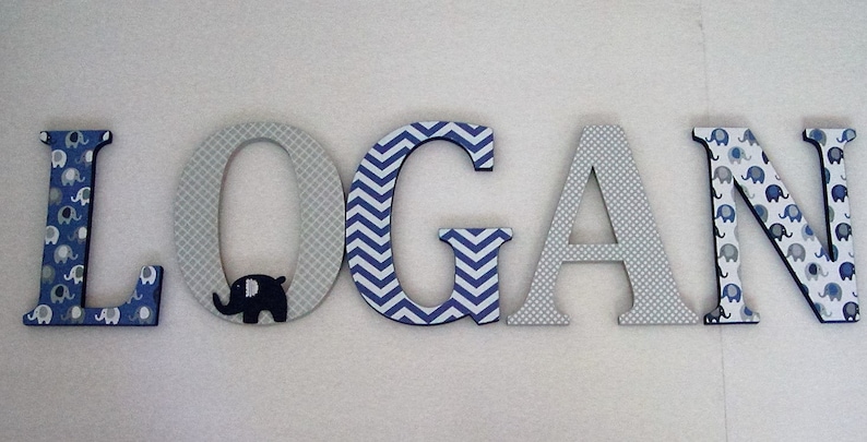 May include: Wooden letters spelling the name "LOGAN" in blue and gray. The letters are decorated with different patterns, including elephants, polka dots, and chevron stripes.