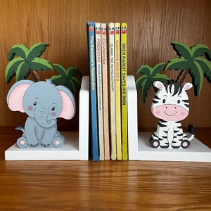 Peut inclure: Des serre-livres en bois blanc avec un &eacute;l&eacute;phant et un z&egrave;bre peints. L'&eacute;l&eacute;phant est gris avec des oreilles roses et est assis sur une base blanche. Le z&egrave;bre est noir et blanc avec un nez rose et est assis sur une base blanche. Les serre-livres tiennent une rang&eacute;e de livres pour enfants color&eacute;s avec des titres comme "Pinocchio", "Cendrillon" et "Dumbo l'&eacute;l&eacute;phant volant".