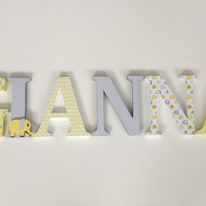 May include: Wooden letters spelling the name "GIANNA" in yellow and gray. The letters are decorated with different patterns, including elephants, chevron, and polka dots.