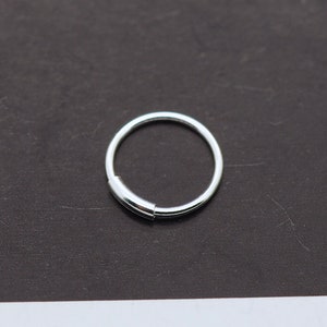 May include: A silver hinged hoop earring. The earring has a simple, circular design with a small, rectangular clasp. The earring is shown against a dark background.