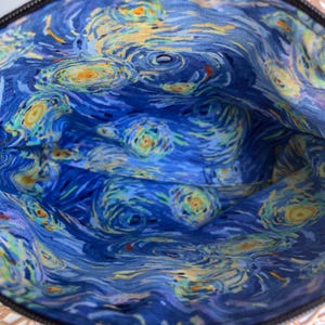 Puede incluir: El interior de una bolsa o estuche est&aacute; forrado con una tela azul con un patr&oacute;n de remolino que recuerda a la pintura "La noche estrellada" de Vincent van Gogh.