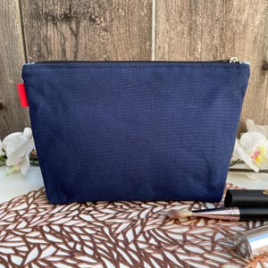 Puede incluir: Una bolsa de lona azul oscuro con cremallera y un tirador de cremallera rojo. La bolsa est&aacute; sobre una superficie decorativa.