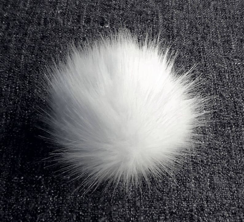 May include: A fluffy white pom pom made of faux fur. The pom pom is round and has a soft, fuzzy texture.
