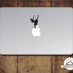 May include: A black silhouette of a dancer standing on top of a white apple logo. The logo is on a silver laptop.