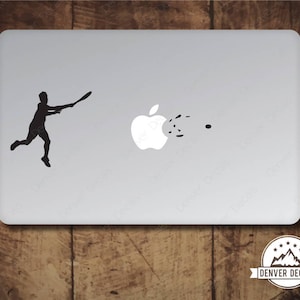 Peut inclure: Un autocollant pour ordinateur portable noir et blanc représentant la silhouette d'une personne jouant au tennis avec un logo de pomme croquée en arrière-plan. L'autocollant est conçu pour un ordinateur portable et porte le texte "Denver Decals".