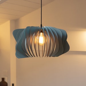 May include: A pendant light fixture featuring a series of curved, slate blue slats arranged in a circular, layered pattern around a central glowing light bulb, suspended from the ceiling by a thin black cord in a room with soft lighting.