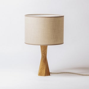 May include: A wooden table lamp with a beige linen lampshade. The lamp has a simple, modern design with a turned wooden base.