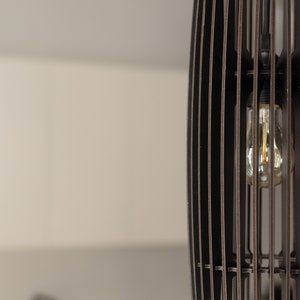 May include: A cylindrical pendant light fixture constructed from vertical dark brown wooden slats arranged in a cage-like pattern. A single clear glass light bulb with a visible filament is suspended inside the center of the slatted structure.