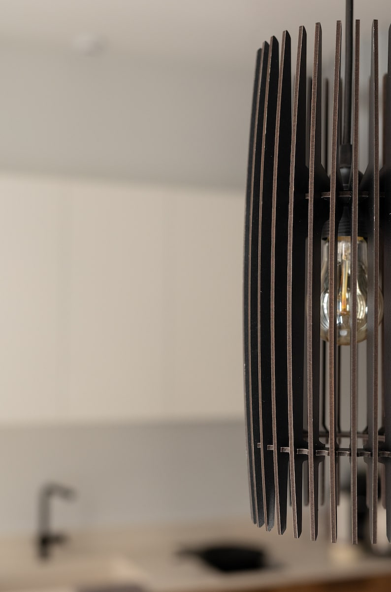 May include: A cylindrical pendant light fixture constructed from vertical dark brown wooden slats arranged in a cage-like pattern. A single clear glass light bulb with a visible filament is suspended inside the center of the slatted structure.