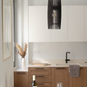May include: A cylindrical pendant light fixture constructed from thin, vertical dark brown wooden slats arranged in a cage-like pattern, suspended by a black cord from the ceiling, featuring a single exposed light bulb visible in the center.