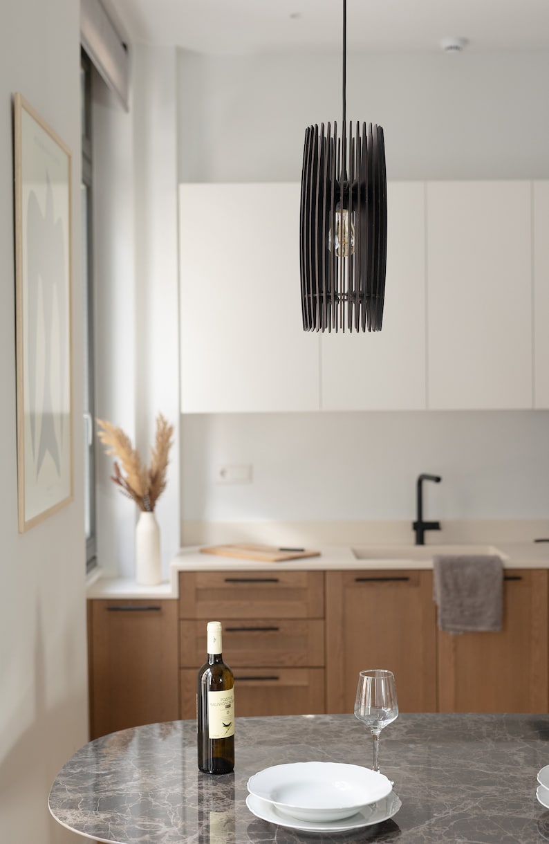 May include: A cylindrical pendant light fixture constructed from thin, vertical dark brown wooden slats arranged in a cage-like pattern, suspended by a black cord from the ceiling, featuring a single exposed light bulb visible in the center.