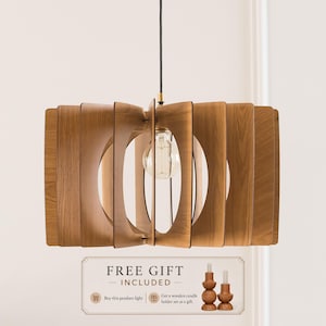 Puede incluir: Una lámpara colgante que presenta una serie de listones de madera verticales y curvados dispuestos en un patrón circular alrededor de una bombilla de cristal transparente. La lámpara cuelga de un cable negro fino y tiene un casquillo metálico.