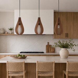 K&ouml;nnte beinhalten: Drei tropfenf&ouml;rmige Pendelleuchten mit einem Design aus h&ouml;lzernen Lamellen. Jede Leuchte h&auml;ngt an einem d&uuml;nnen schwarzen Kabel und zeigt eine sichtbare Gl&uuml;hbirne innerhalb der offenen Struktur &uuml;ber einer K&uuml;cheninsel mit geflochtenen St&uuml;hlen.