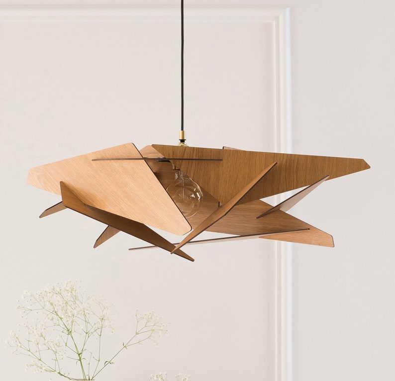 May include: A wooden pendant light fixture with a geometric design. The light fixture is made of multiple pieces of wood that are arranged in a starburst pattern. The light fixture is suspended from the ceiling by a black cord.