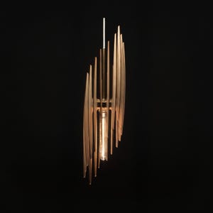 Op de afbeelding: Een verticale hanglamp met een reeks dunne, lichtgekleurde houten latten die in een gelaagde, langwerpige structuur zijn gerangschikt. Een enkele, heldere, buisvormige Edison-gloeilamp hangt in het midden en verspreidt een warme gloed.