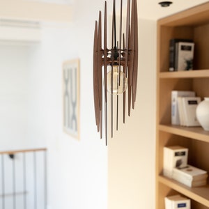 May include: A wooden pendant light fixture with a geometric design. The light is hanging from a black cord and has a clear light bulb.