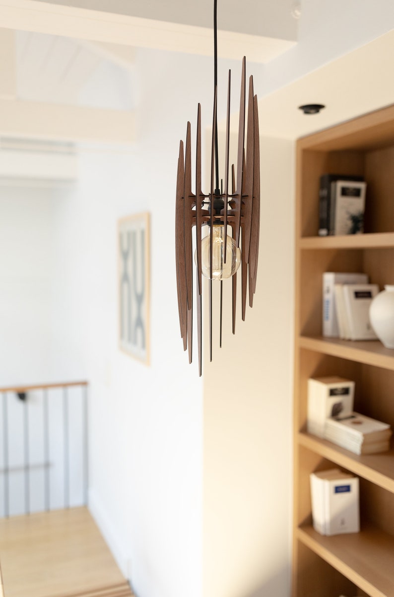 May include: A wooden pendant light fixture with a geometric design. The light is hanging from a black cord and has a clear light bulb.