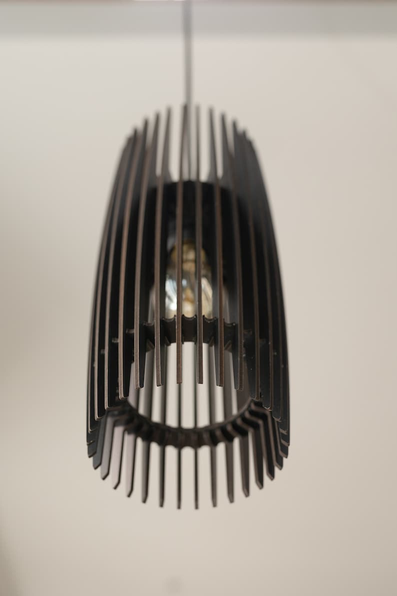 May include: A dark brown pendant light fixture featuring a cylindrical cage design composed of vertical slats. The structure is suspended from a thin cord and contains a single light bulb visible through the open gaps between the wooden slats.