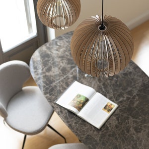 Pu&ograve; includere: Due lampade a sospensione sferiche realizzate con sottili listelli di legno marrone chiaro disposti a raggiera. Ogni lampada presenta un'apertura centrale ed &egrave; sospesa tramite un sottile cavo nero fissato al soffitto sopra un tavolo.