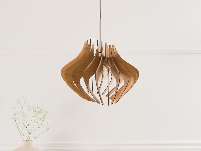 May include: A pendant light fixture featuring a series of curved, light brown wooden slats arranged in a symmetrical, organic shape. The structure hangs from a thin black cord and contains a single exposed light bulb in the center.