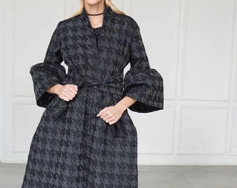 May include: A black and grey houndstooth patterned coat with a tie belt and long sleeves. The coat has a slightly flared silhouette.