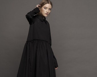 Könnte beinhalten: Ein schwarzes, langärmliges Kleid mit einem gerafften Rock und einem Kragen. Das Kleid wird mit schwarzen Schnürstiefeletten getragen.