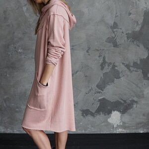 May include: A long, pink hooded sweatshirt dress with a raw hem and two pockets. The dress is made of a soft, comfortable fabric and is perfect for casual wear.