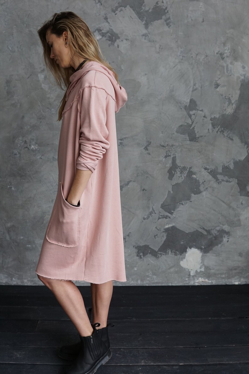May include: A long, pink hooded sweatshirt dress with a raw hem and two pockets. The dress is made of a soft, comfortable fabric and is perfect for casual wear.
