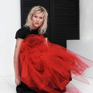 May include: A woman wearing a black top and a red tulle skirt. The skirt is very full and billows out around her.