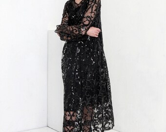 May include: A black sequined midi dress with a long sleeve and a lace overlay. The dress has a loose fit and a round neckline.