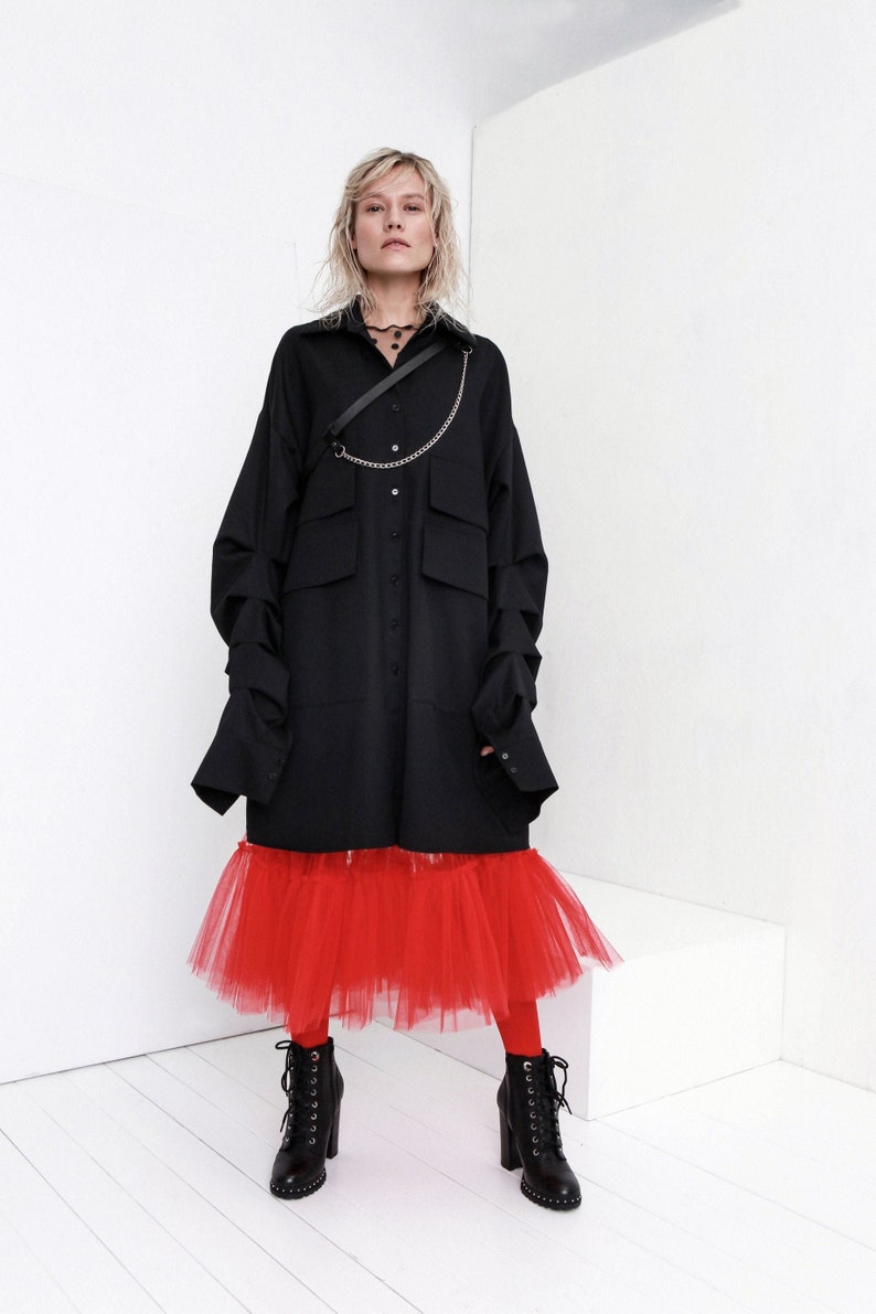 Op de afbeelding: Een zwart oversized shirt met een kettingdetail en een rode tule rok. Het model draagt zwarte enkellaarsjes.