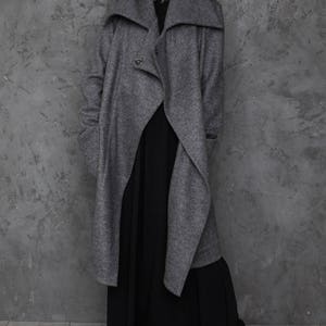 Pu&ograve; includere: Un cappotto grigio a maniche lunghe con un ampio colletto ripiegato e una chiusura con un solo bottone. Il cappotto &egrave; indossato sopra un abito maxi nero.