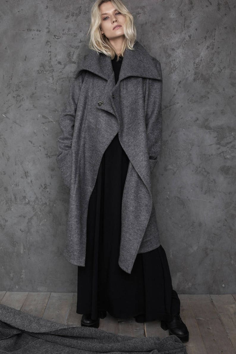 Pu&ograve; includere: Un cappotto grigio a maniche lunghe con un ampio colletto ripiegato e una chiusura con un solo bottone. Il cappotto &egrave; indossato sopra un abito maxi nero.
