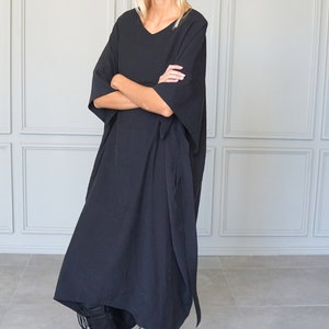 May include: A black, loose-fitting, long-sleeved dress with a v-neckline. The dress is worn with black lace-up boots.