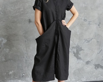 Puede incluir: Mono negro de lino con mangas cortas, bolsillos delanteros grandes y cuello camisero. La modelo lleva un sombrero negro, gafas de sol y botas de combate negras. El conjunto está diseñado para una estética moderna y minimalista.